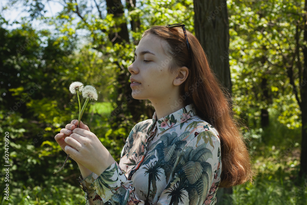 a close-up photo of a happy, cute woman with red hair holding dandelions in her hand and blowing them up while walking in the park on a sunny day a close-up photo of a happy, cute woman with red hair holding dandelions in her hand and blowing them up while walking in the park on a sunny day
