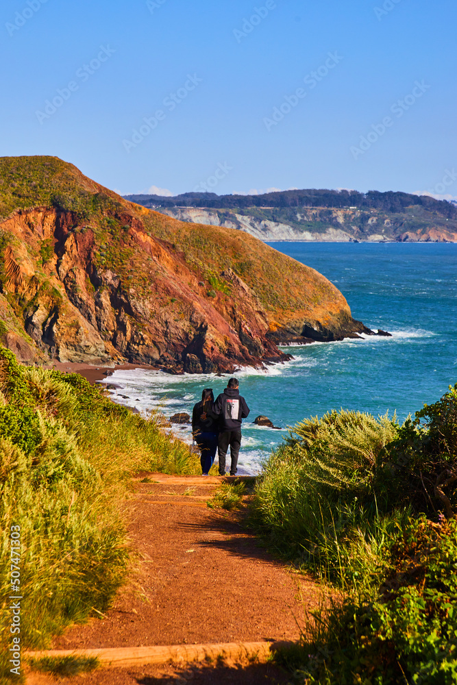 Fototapeta premium Couple on trail leading to beautiful ocean beaches next to hills