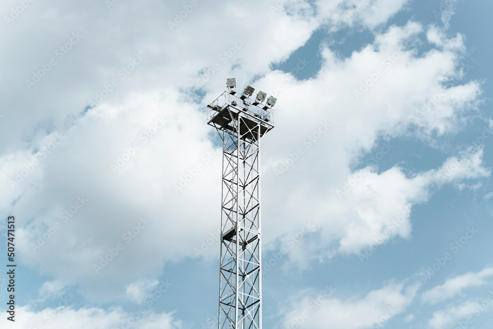 High lighting tower with spotlights against cloudy blue sky outdoors