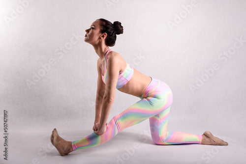 A beautiful slender gymnast in a stretch in a tracksuit does sports or yoga in the studio