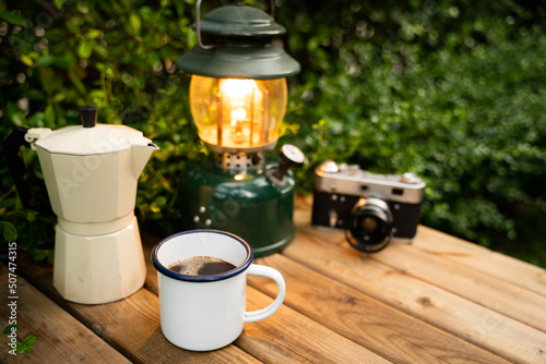 Selective focus white enamel coffee mug and coffee set in the garden with ancient lanterns in a camping atmosphere.