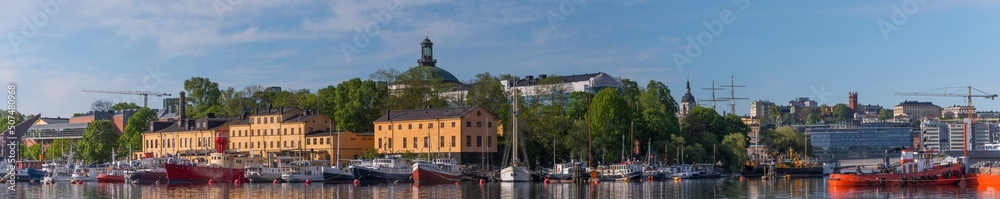 Panorama view over motor boats at piers in the islands Skeppsholmen and Blasieholmen, old military buildings and the district Södermalm in the background a sunny summer day in Stockholm