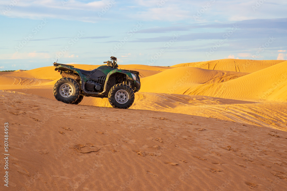 Quadracycle stands among the yellow sand dunes in the Sahara desert under the blue sky in Tunisia. Desert quad bike racing. Travel landscape with copy space Quadracycle stands among the yellow sand dunes in the Sahara desert under the blue sky in Tunisia. Desert quad bike racing. Travel landscape with copy space