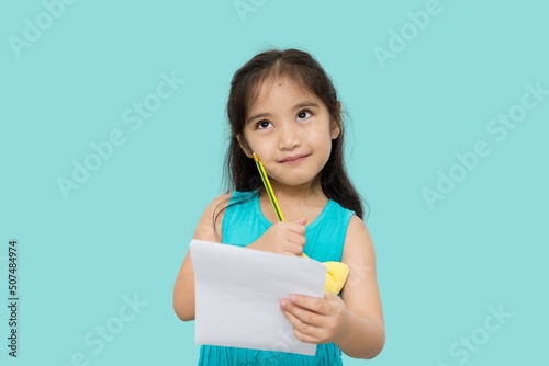 Little Asian girl having paper and pencil in hands looking up, writer waiting for muse, isolated on green background
