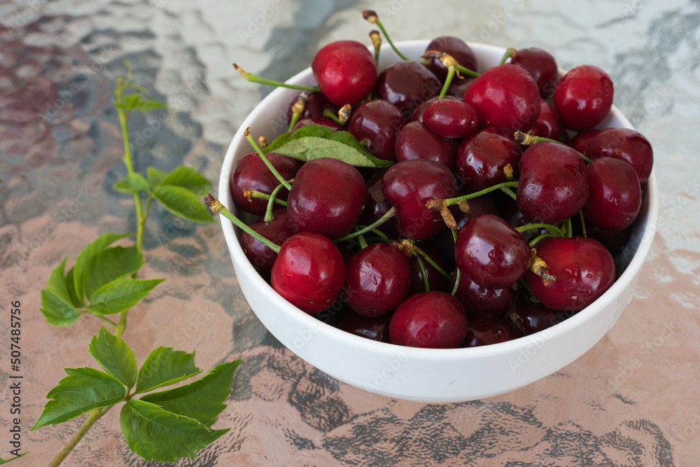 Ripe red cherries in a bowl and next to it on wooden table Ripe red cherries in a bowl and next to it on wooden table