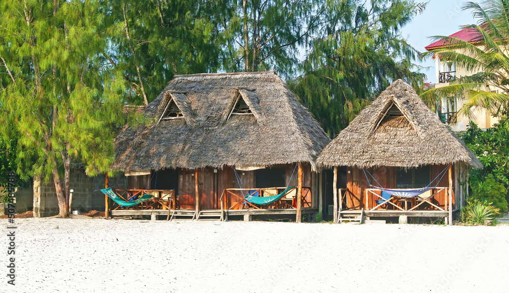 Paje, Zanzibar - December 9. 2007: Beautiful idyllic sand beach with typical basic wood bamboo sea bungalows, hammocks, trees at seaside resort