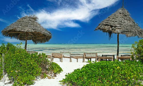 Beautyful empty idyllic lonely bright white sand beach, 2 thatch umbrellas, row of wooden basic sun beds, turquoise water, clear blue sky - Paje, Zanzibar photo