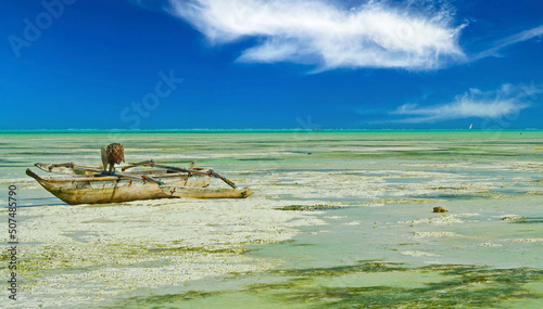 Beautiful lonely tropical beach landscape, white sand low tide ebb mudflat, on single stranded traditional dau wood boat, clear blue sky horizon - Paje, Zanzibar
