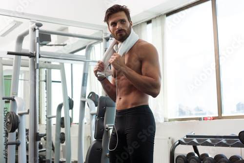 Young fit man in gym, fitness, listening to music, with towel, lifting weights