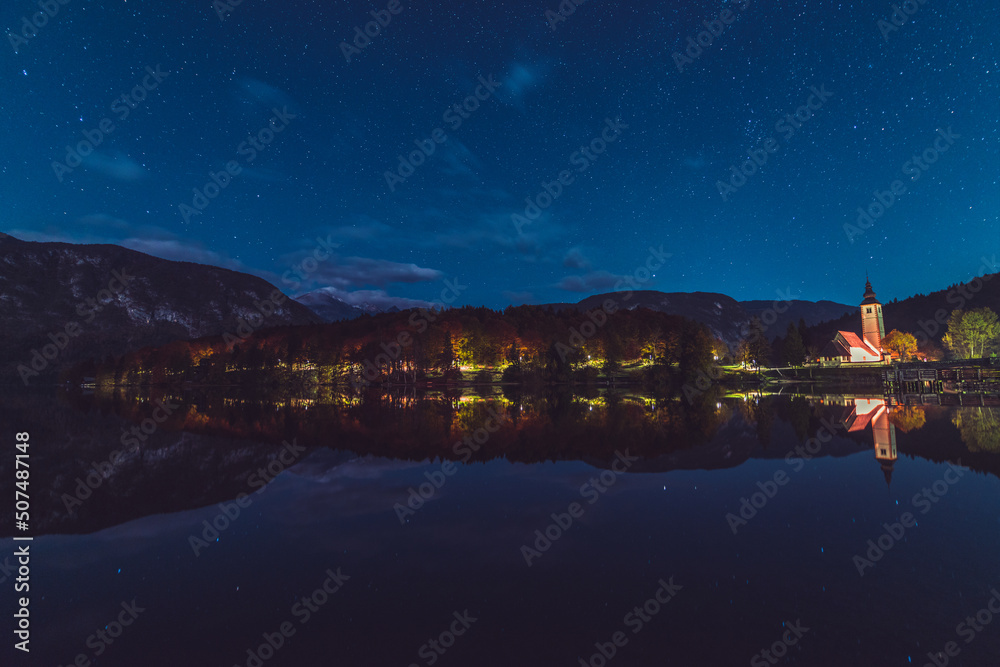 Night reflections of the church, bridge and autumn forest in the lake Bohinj