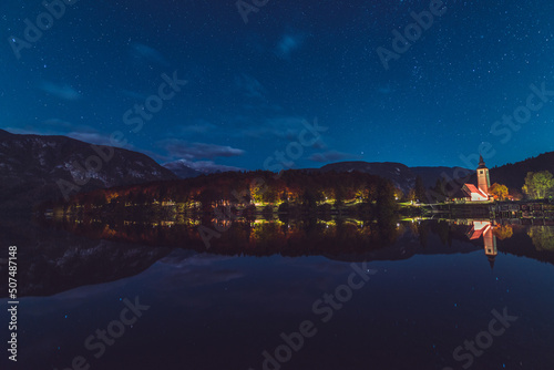 Night reflections of the church, bridge and autumn forest in the lake Bohinj