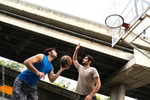 Two caucasian men pratice baskegball in court at urban street. photo