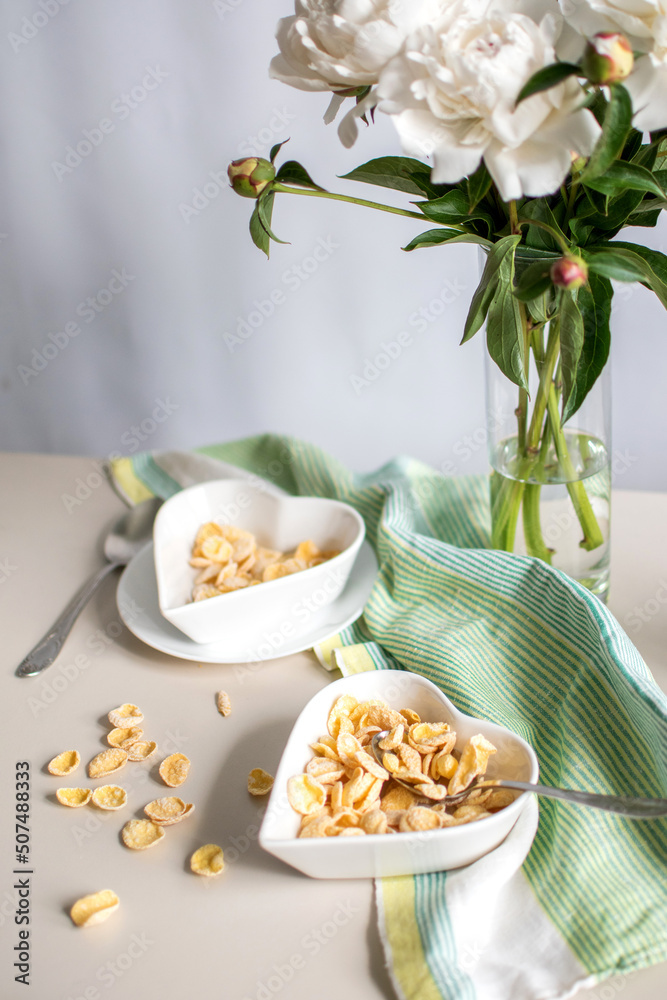 Breakfast with milk and cornflakes. white dishes and peonies on the table. Breakfast with milk and cornflakes. white dishes and peonies on the table.