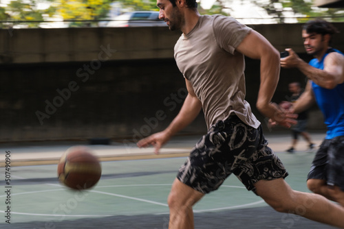 Young causian basketball player shooting ball on street court.