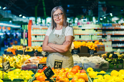 Billede på lærred portrait of a senior gray-haired woman of a supermarket worker, worker spreads f