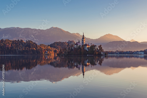 Lake Bled at Sunrise. Church, castle and the mountains are basking in the morning sun