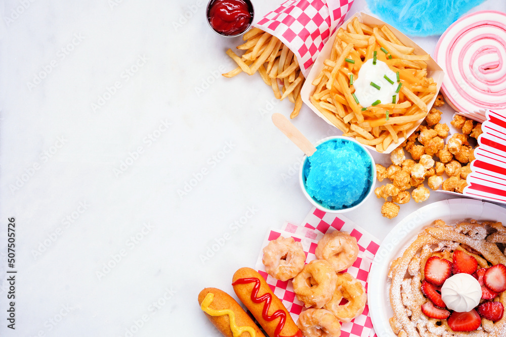 Carnival theme food side border on a white marble background. Above view with copy space. Summer fair concept. Corn dogs, funnel cake and snacks.