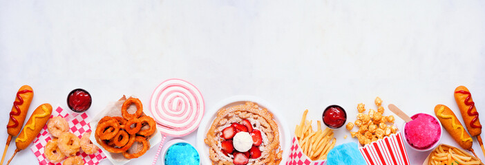 Carnival theme food bottom border on a white marble background. Top view with copy space. Summer fair concept. Corn dogs, funnel cake and snacks.