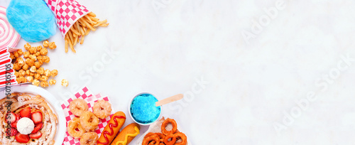 Carnival theme food corner double on a white marble background. Overhead view with copy space. Summer fair concept. Corn dogs, funnel cake and snacks.