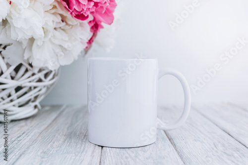 White cup mockup on background with peony bouquet on white table.