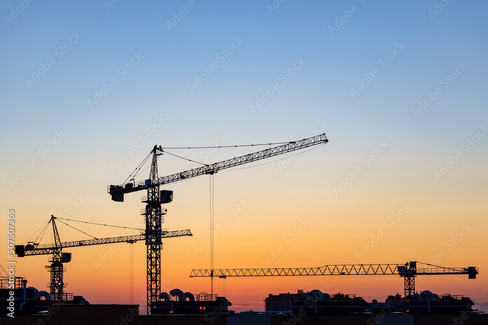 Silhouettes of tower cranes on construction site at sunset Silhouettes of tower cranes on construction site at sunset