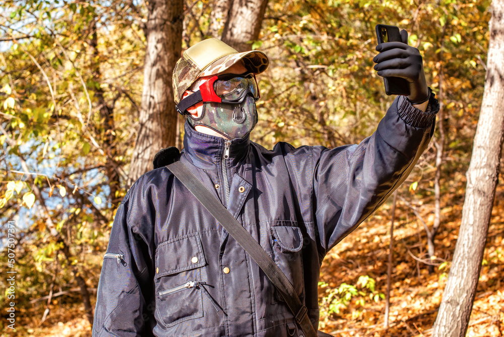 A man wearing respirator mask and dialing a smartphone walking in the forest at COVID-19 period. A man wearing respirator mask and dialing a smartphone walking in the forest at COVID-19 period.