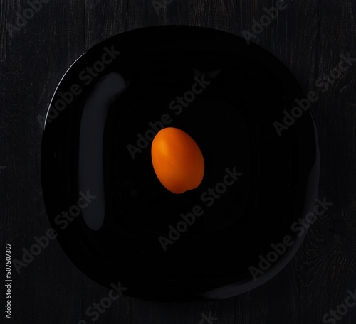orange tomato placed in the center of a black plate