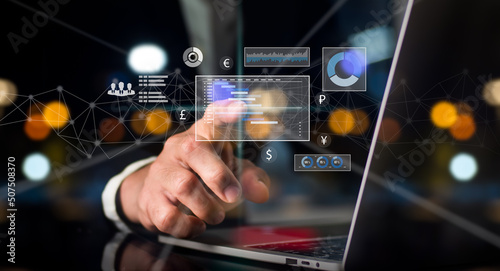 On his left hand, a man in a suit holds a cell phone. On a rapidly expanding stock chart, his right hand point. Background of a globe with hazy lights