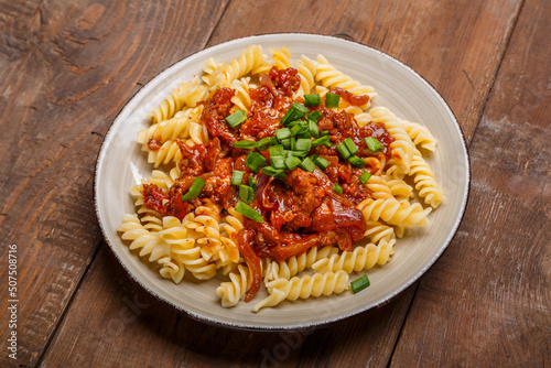 Beige plate with bolognese pasta on a wooden table sprinkled with green onions.