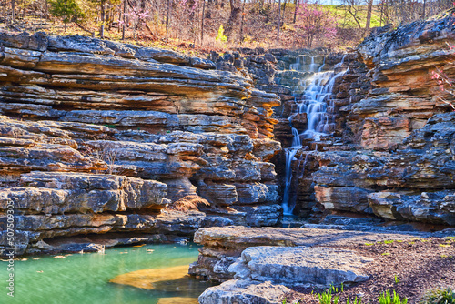 Jagged rocks featuring simple waterfall into teal waters photo