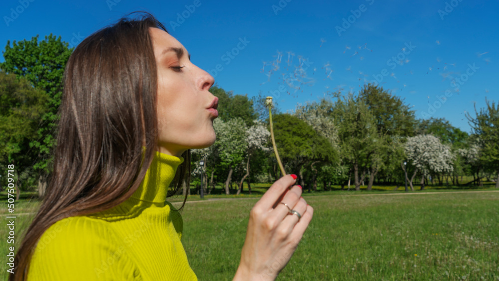 Beautiful young woman blowing a dandelion. Girl with dandelion in hand. Allergic to pollen of flowers. Spring allergy. Beautiful young woman blowing a dandelion. Girl with dandelion in hand. Allergic to pollen of flowers. Spring allergy.