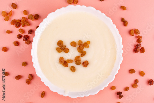Semolina porridge with delicious brown raisins in a white plate (bowl) on a pink background, close-up, top view. Cereals contain gluten.