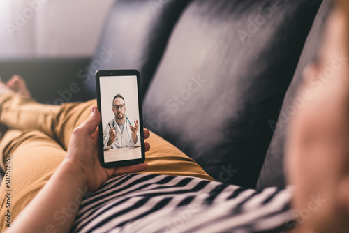Woman lying on a sofa and talking with a doctor online using mobile phone. Telemedicine concept.