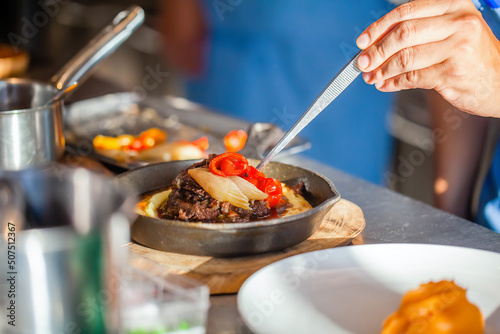 Close up of chef hands in luxury hotel or restaurant kitchen decorating dish. Preparing beef steak, decorate dish. Modern kitchen with utensils. 