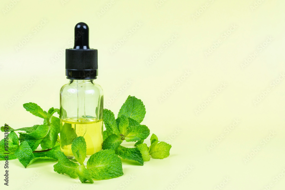 Essential oil of fragrant mint (peppermint) in a glass bottle with a pipette on a yellow background. Space for text. Aromatherapy (against fatigue, headache, relaxation), spa, skin care. Essential oil of fragrant mint (peppermint) in a glass bottle with a pipette on a yellow background. Space for text. Aromatherapy (against fatigue, headache, relaxation), spa, skin care.