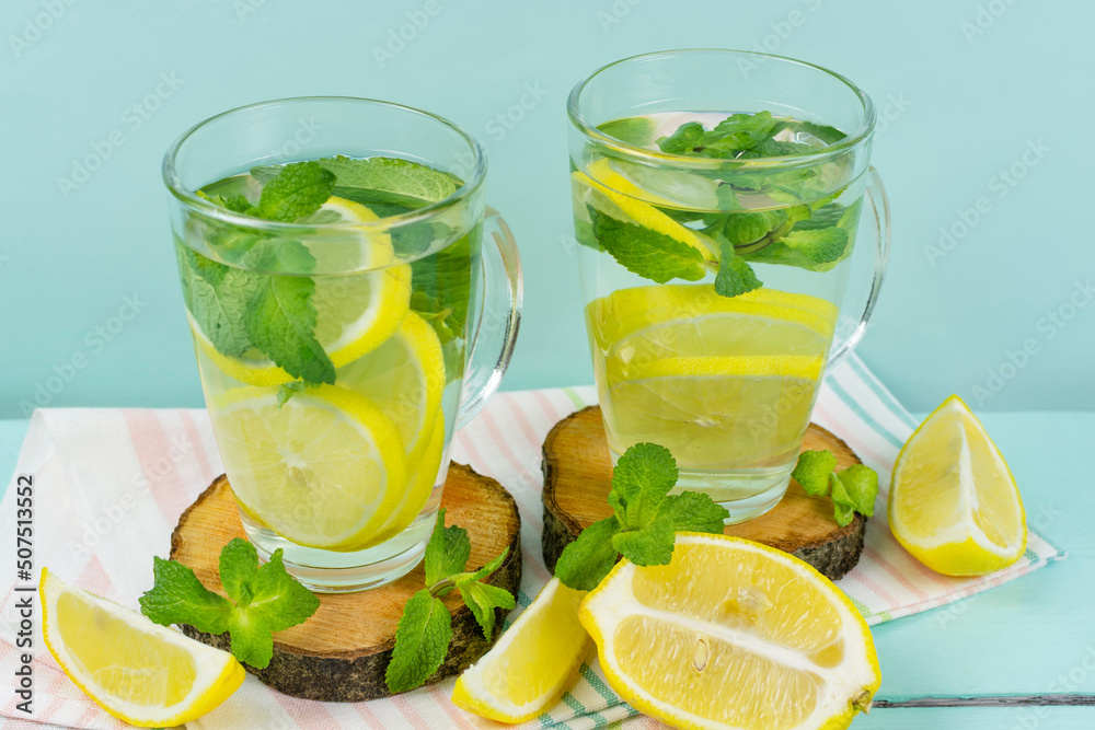 Lemon drink with mint in two glass glasses with a handle on a blue background. Proper nutrition, healthy lifestyle. Detox, fruit water, lemonade, vitamin C. Lemon drink with mint in two glass glasses with a handle on a blue background. Proper nutrition, healthy lifestyle. Detox, fruit water, lemonade, vitamin C.