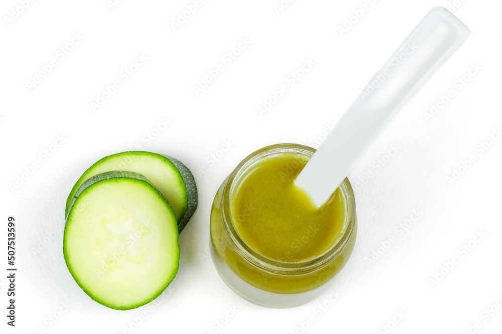 A glass jar of baby squash puree (zucchini) with a spoon on a white insulated background. Top view. Baby food. The first lure of the baby. A glass jar of baby squash puree (zucchini) with a spoon on a white insulated background. Top view. Baby food. The first lure of the baby.