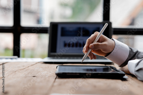 Person holding pen pointing at tablet placed on desk, business man looking at information on tablet and using tablet to communicate with company team through messaging and email programs.