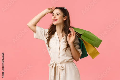 Romance, shoppaholic and women concept. Cheerful tender feminine woman holding shopping bags behind back, taking-off glasses and smiling happily left, enjoy browsing stores photo