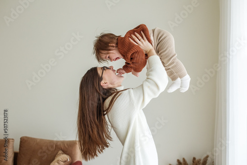 Happy cheerful young mother throws an adorable baby in air, plays, hugs baby with love, care photo