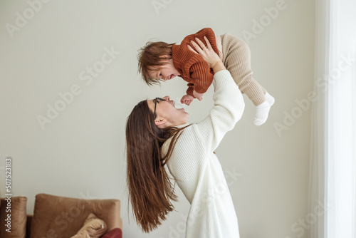Happy cheerful young mother throws an adorable baby in air  plays  hugs baby with love  care