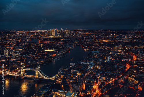 Aerial night view of Tower Bridge over river Thames, illuminated buildings glowing in dark