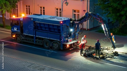A team of road builders perform road repairs at night with the help of a large truck vacuum cleaner. Professional repairmen change the manhole on the roadway. photo