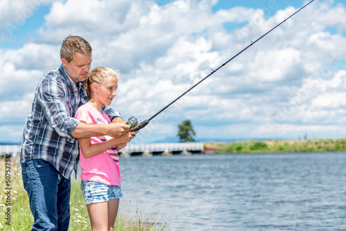 A father and daughter fishing together on a river bank on a beautiful summer day.
