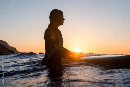 Surfer girl waiting for a wave in the water at sunset