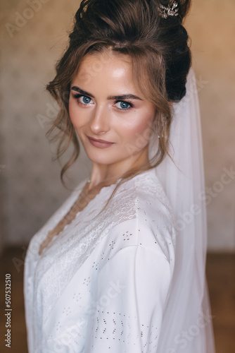 The bride in a white peignoir with delicate makeup and hair, final preparations for the ceremony. © Ivan
