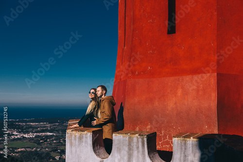 a dreamy couple walks around the Pena National Palace, stands on a balcony and poses against the backdrop of a red wall and a beautiful landscape., photo