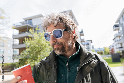 Mature man with grey hair in blue sunglasses holding coffee beaker