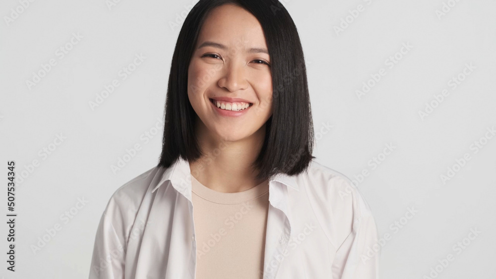 Beautiful girl looking at camera and sincerely smiling. Asian woman standing over white background Beautiful girl looking at camera and sincerely smiling. Asian woman standing over white background