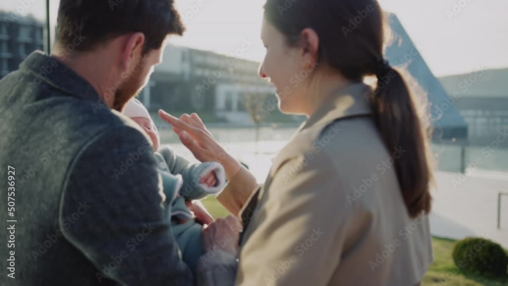 Attractive father holding new born baby in hands near mother and playing together. Smiling feel happy at sunlight. Outdoors on street